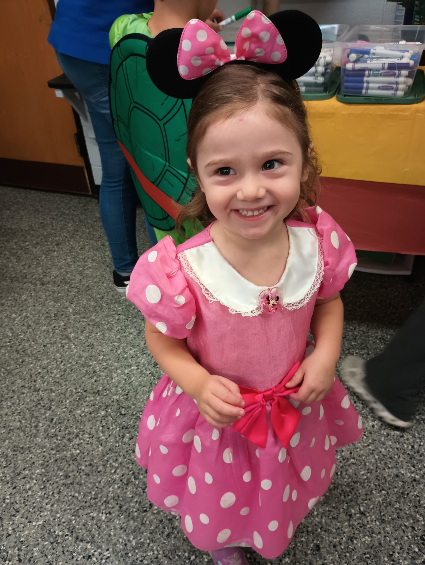 A young girl in a Minnie Mouse costume smiles.